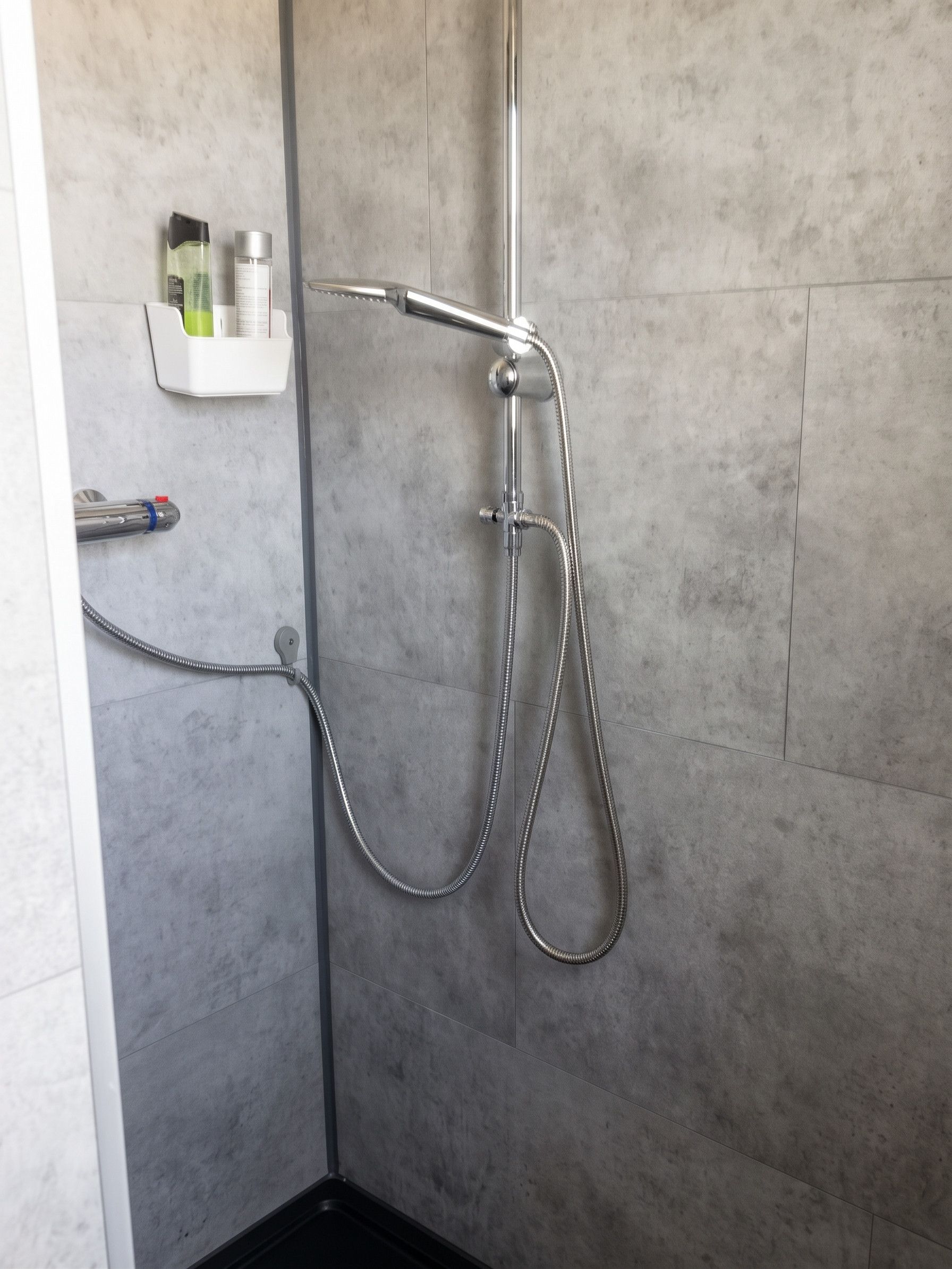 Eine Dusche mit Handbrause und flexiblen Schlauch, an einer gefliesten Wand befestigt.
