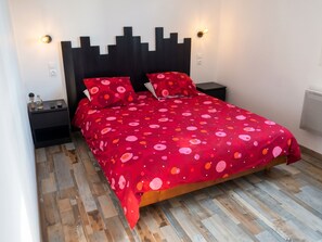 A bed with a red patterned bedspread, two pillows, a dark headboard, and a nightstand with a lamp.