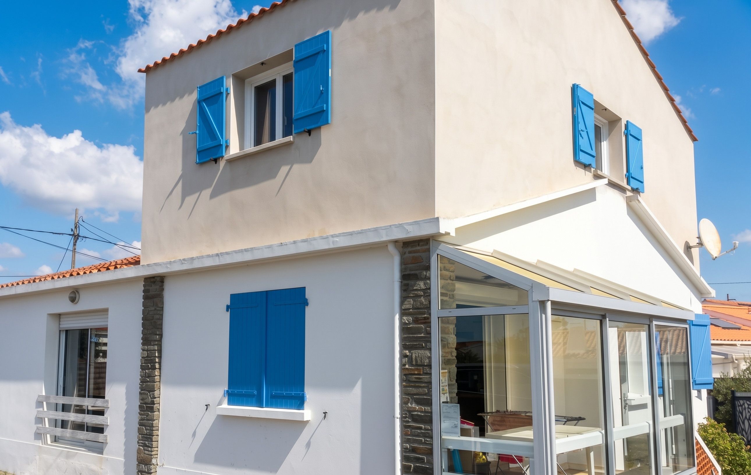 Ein zweistöckiges Gebäude mit blauen Fensterläden, einer Stein-Fassade und einem Glasbalkon.
