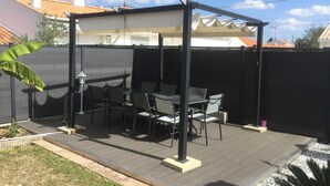 Een terras buiten met een overdekte zithoek, een houten terras en een zwarte omheining.