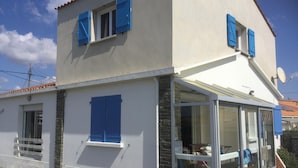 Een gebouw met twee verdiepingen, blauwe luiken, een glazen deur en een schotelantenne.