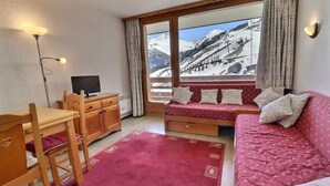 Una habitación acogedora con un escritorio de madera, un sofá rojo y un amplio ventanal con vista a una montaña nevada.