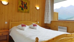 Un dormitorio con paneles de madera, una cama, dos almohadas, una mesita de noche, una lámpara de pared y una ventana con vistas a la montaña.