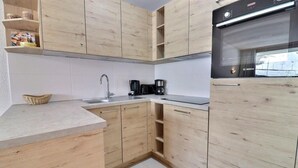 A modern kitchen with wooden cabinets, a built-in oven, and a coffee maker. - 10m from ski slopes, 4th floor, balcony, 40m², Méribel-Mottaret (Méribel - Les Allues)