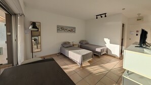 Quarto com duas camas de solteiro, uma escrivaninha com computador, um espelho e um quadro na parede.