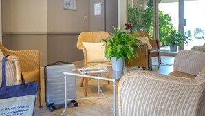 Um saguão de hotel com móveis de vime, uma mesa de vidro, uma planta em vaso e um letreiro com informações de contato.