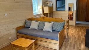 A cozy room with a wooden sofa, a small wooden table, and a window with a view of the outside. - Bright 2-Room with Balcony and WIFI - Village Center (Brides-les-Bains)
