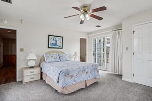 A bedroom with a bed, bedside tables, a ceiling fan, and a view to the outside.