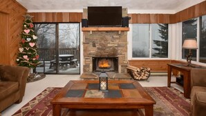 A cozy living room with a stone fireplace, a Christmas tree, and a large window. - True Ski-In/Ski-Out on Comet & Voyager, Sleeps 9, Fireplace, Pet Friendly (Hidden Valley)