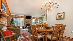 A cozy living room with a fireplace, a dining area with a chandelier, and a large window. - True Ski-In/Ski-Out on Comet & Voyager, Sleeps 9, Fireplace, Pet Friendly (Hidden Valley)