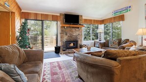 A cozy living room with a stone fireplace, leather sofas, a Christmas tree, and a large window offering a view of the outdoors. - True Ski-In/Ski-Out on Comet & Voyager, Sleeps 9, Fireplace, Pet Friendly (Hidden Valley)