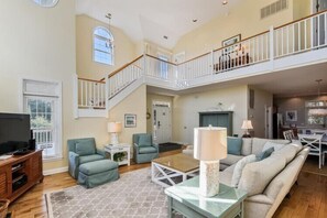 A spacious living room with a high ceiling, a staircase leading to an upper level, and a television on a wooden stand. - About 400ft to Ships Watch Beach Access - Walk to Duck (Duck)