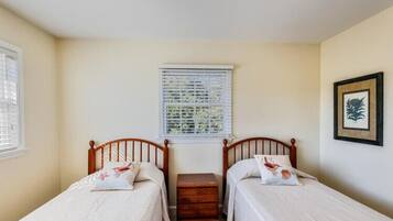 A room with two single beds, a nightstand, a window with blinds, and a framed picture on the wall.