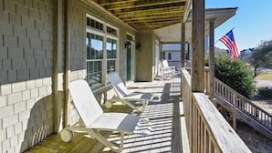 A covered porch with white lounge chairs, a wooden deck, and an American flag.