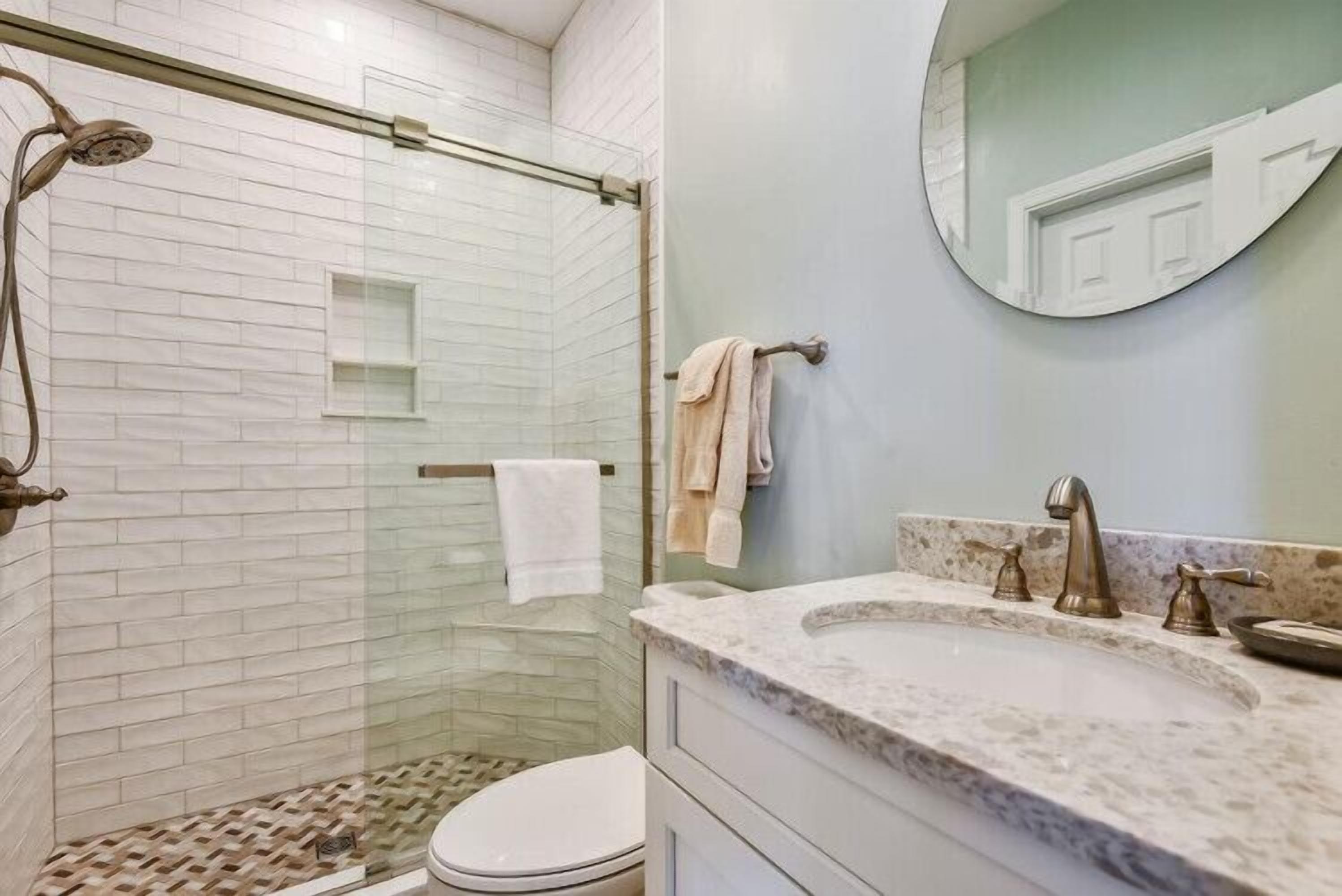 A bathroom with a glass-enclosed shower, a marble sink, and a toilet.