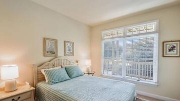 A bedroom with a bed, bedside tables, a window with blinds, and wall-mounted artwork.