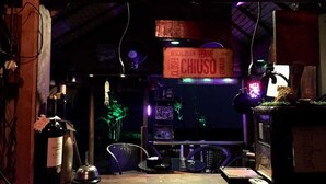 Um espaço de bar com iluminação fraca, um letreiro com a palavra 'CHUSO', uma garrafa de vinho e um letreiro de neon.