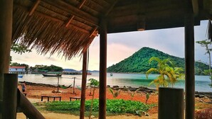 Vista da praia com estrutura de telhado de palha, areia dourada e barcos na água.
