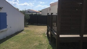 A fenced backyard with a wooden gate, a white building with a blue door, and a clear sky. - Homerez - House/Garden, Saint-Hilaire-de-Riez (Saint-Hilaire-de-Riez)