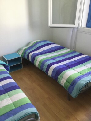 Et lille, enkelt værelse med to senge, et lille bord og et vindue.