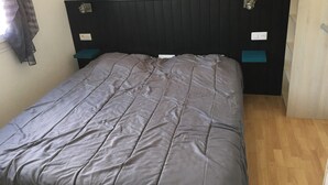A bed with a dark headboard, two bedside tables, and a window with a curtain. - Homerez - House/Garden, Saint-Hilaire-de-Riez (Saint-Hilaire-de-Riez)
