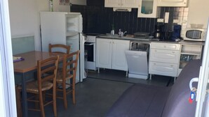 A compact kitchen with white cabinets, a dining table with chairs, and a purple sofa. - Homerez - House/Garden, Saint-Hilaire-de-Riez (Saint-Hilaire-de-Riez)