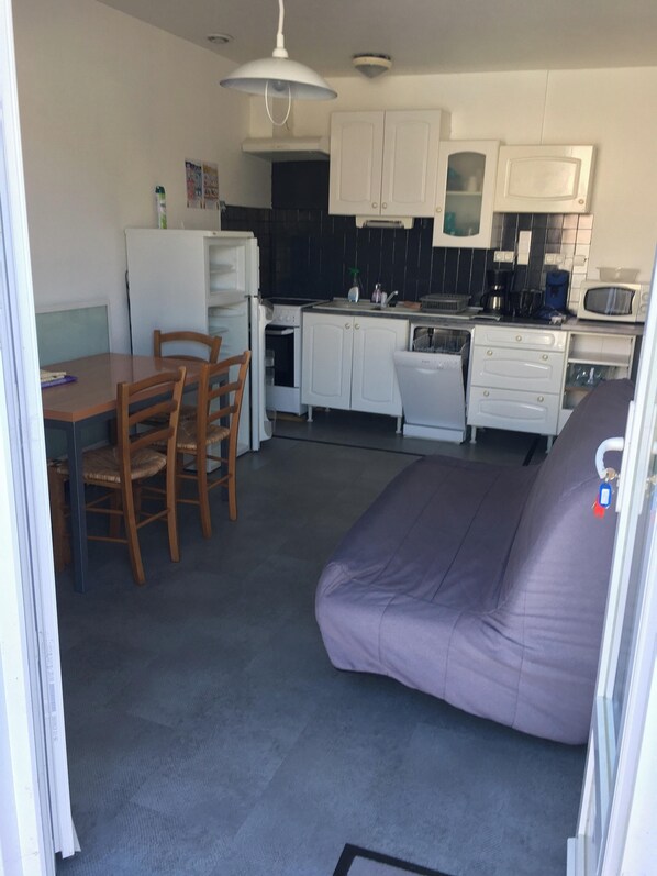 Et kompakt køkken med hvide skabe, et spisebord med stole og en lilla sofa.