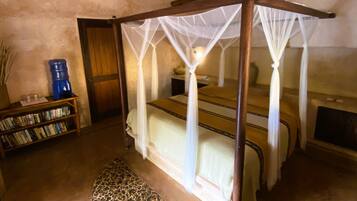 A room with a four-poster bed, a ceiling fan, a bookshelf, and a patterned rug.