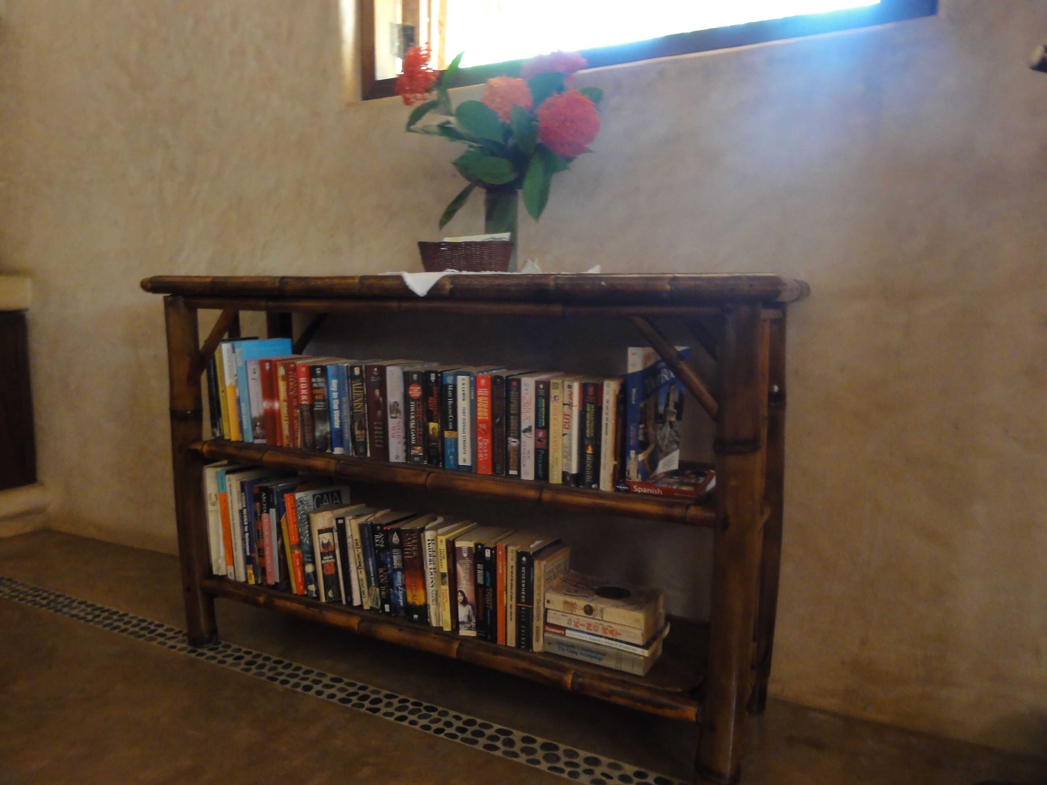 Una estantería de madera con libros y un jarrón de flores.