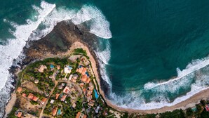 An aerial view of a coastal resort with multiple buildings, a beach, and a large body of water. - Troncones Point Hostel (Troncones)