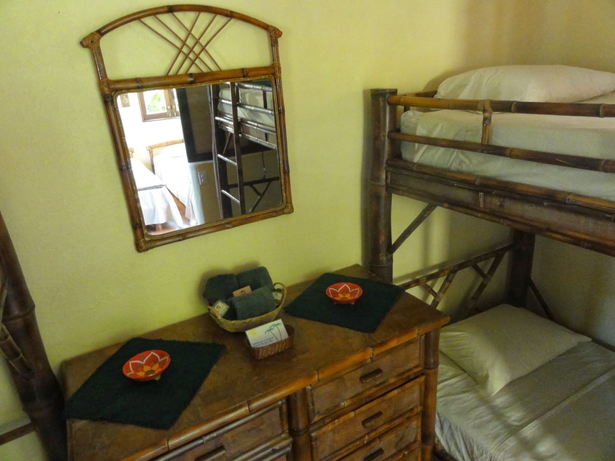 Ein Stockbett mit Holzrahmen, ein Spiegel darüber und eine Kommode mit Schubladen und einem Korb.