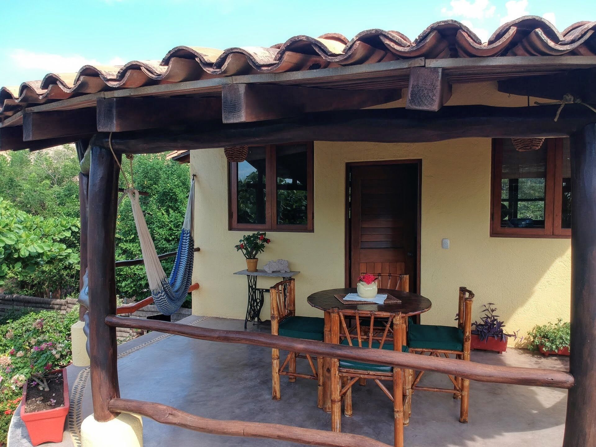 A covered outdoor seating area with a table and chairs, a hammock, and potted plants.