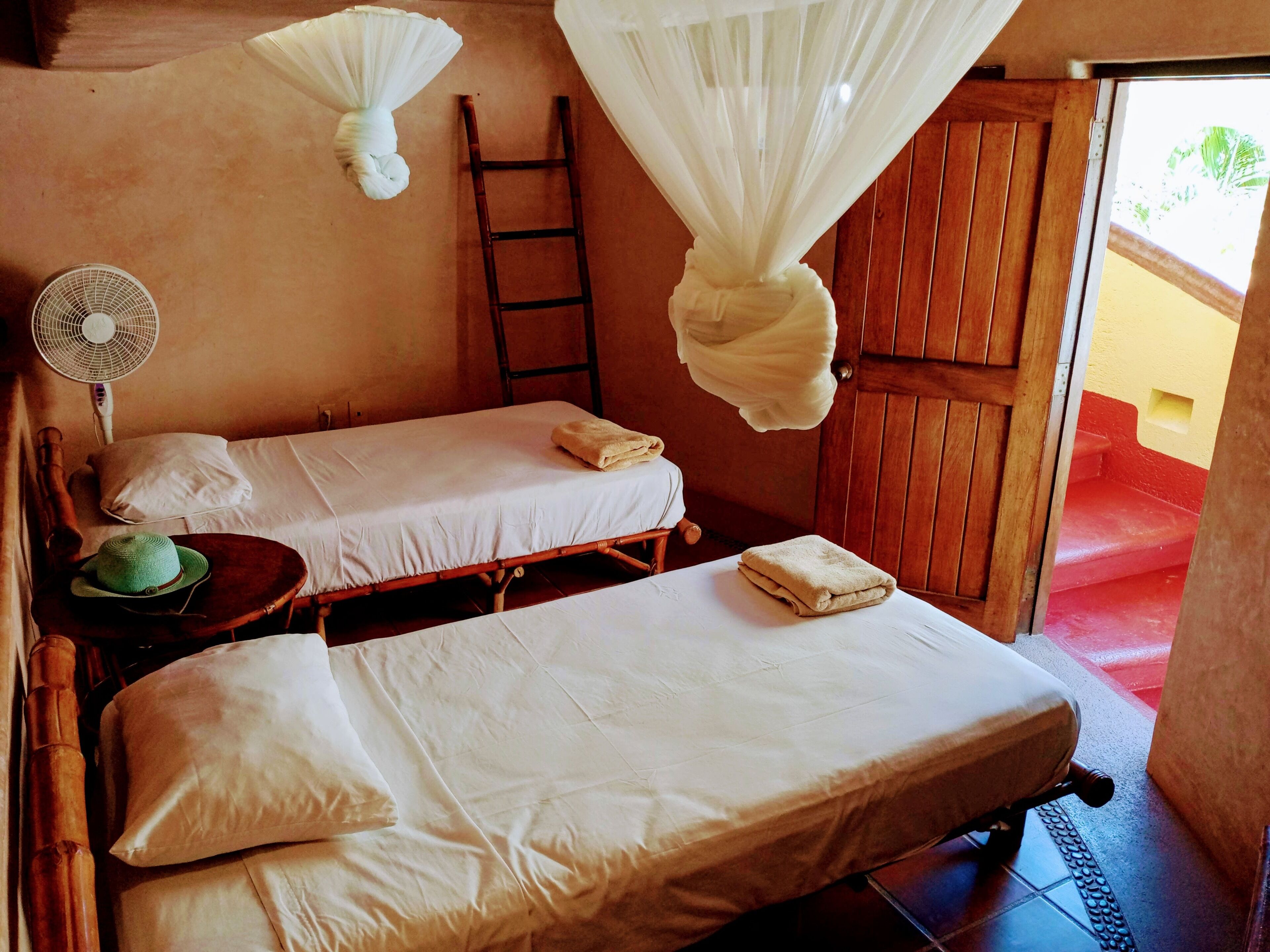 A room with two beds, a fan, a ladder, and a door leading outside.
