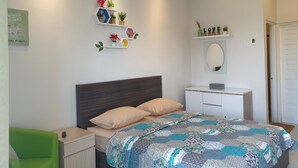 A bedroom with a bed, bedside tables, a green chair, a white dresser, and a wall-mounted shelf with decorative items. - Comfy Room in Piliau Residence (Denpasar)