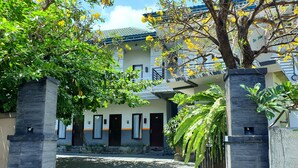A modern building with a gated entrance, a covered walkway, and a balcony with yellow flowers. - Comfy Room in Piliau Residence (Denpasar)
