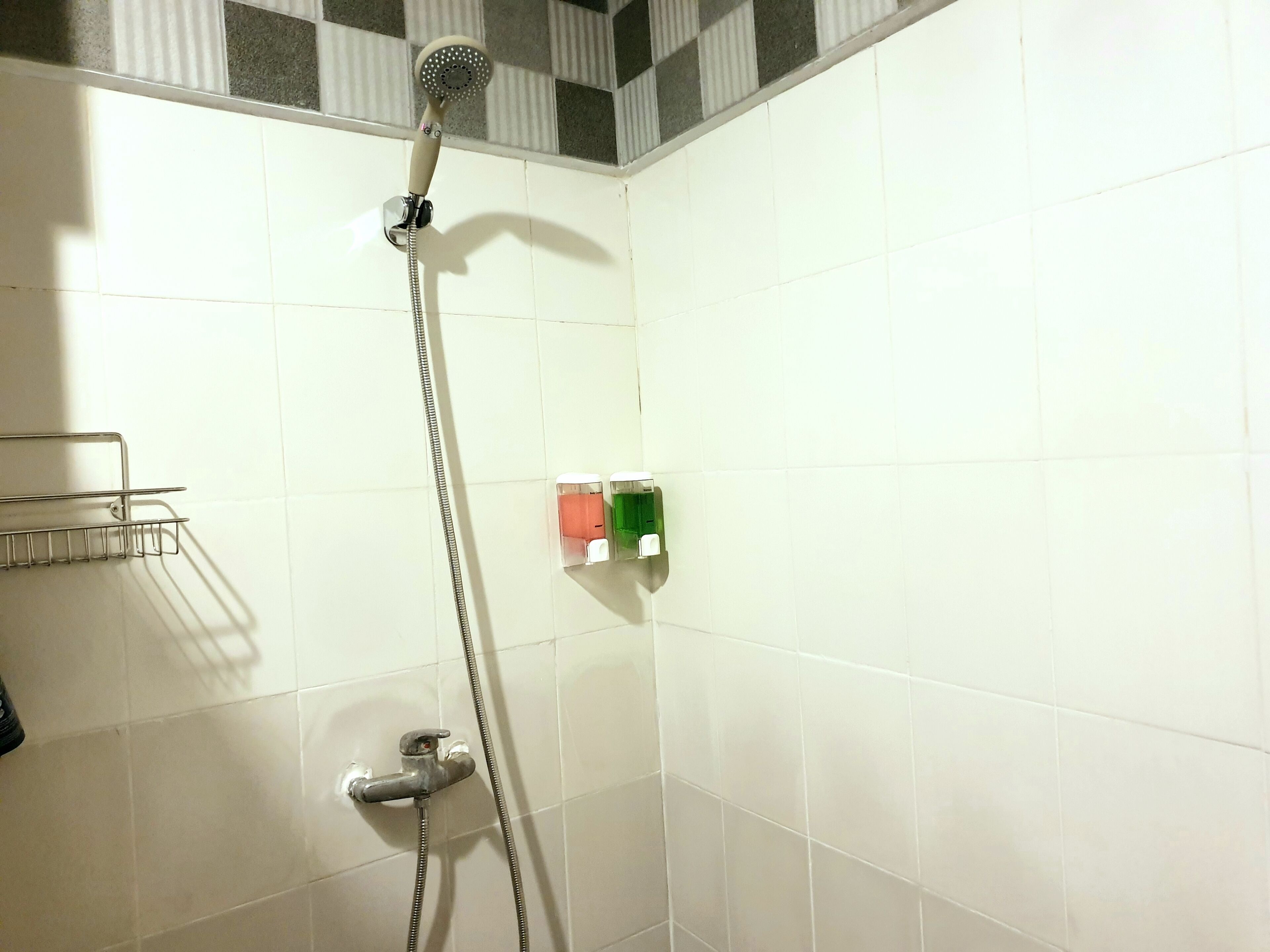 A shower with a handheld showerhead, a wall-mounted faucet, and a soap dispenser.