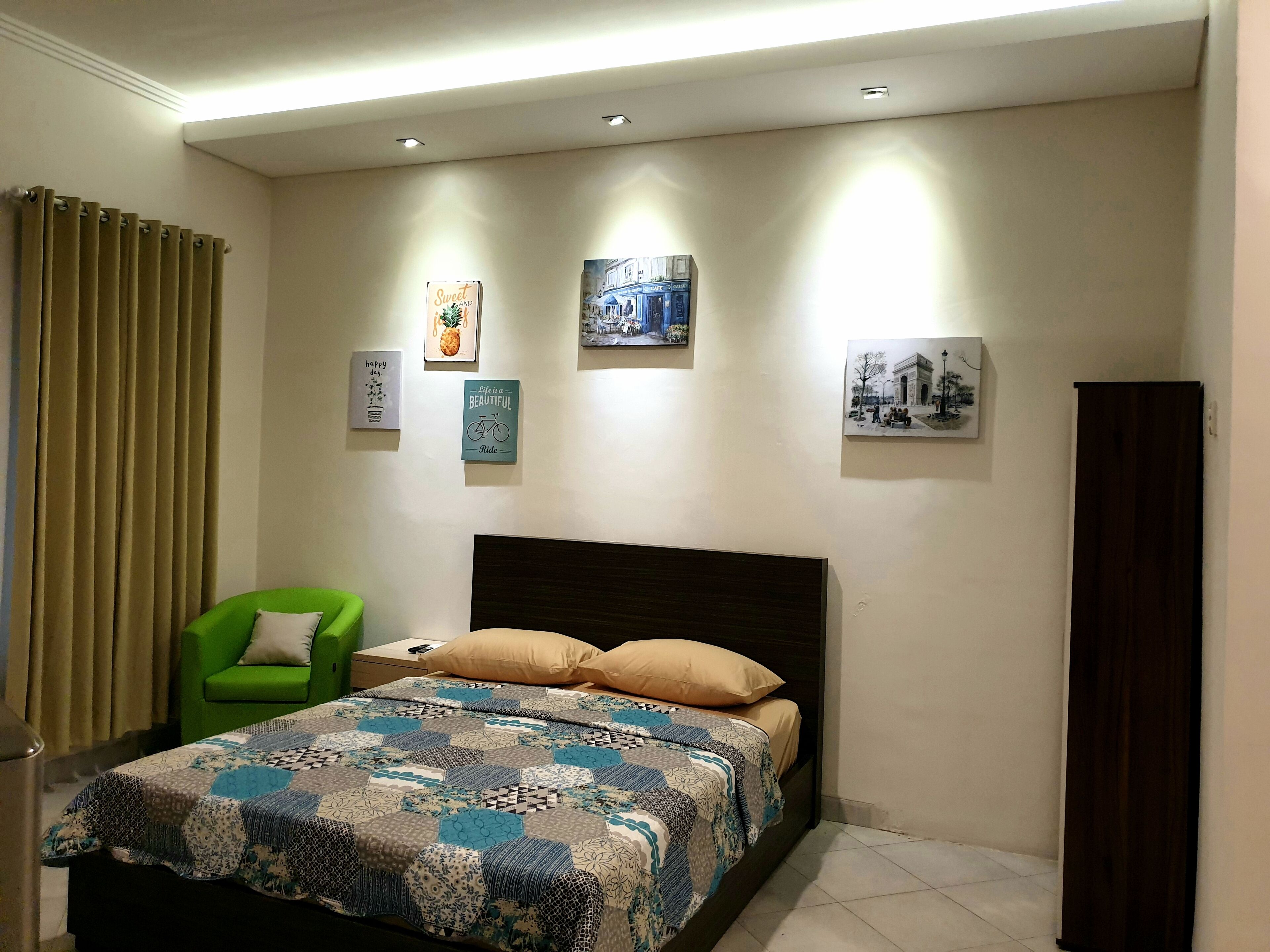 A bedroom with a bed, green chair, and artwork on the wall.