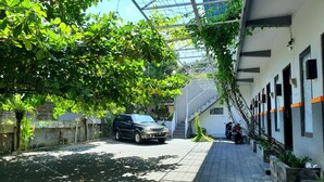 A paved pathway with a parked SUV, a motorcycle, and a staircase leading to a building with multiple windows and a metal fence. - Comfy Room in Piliau Residence (Denpasar)
