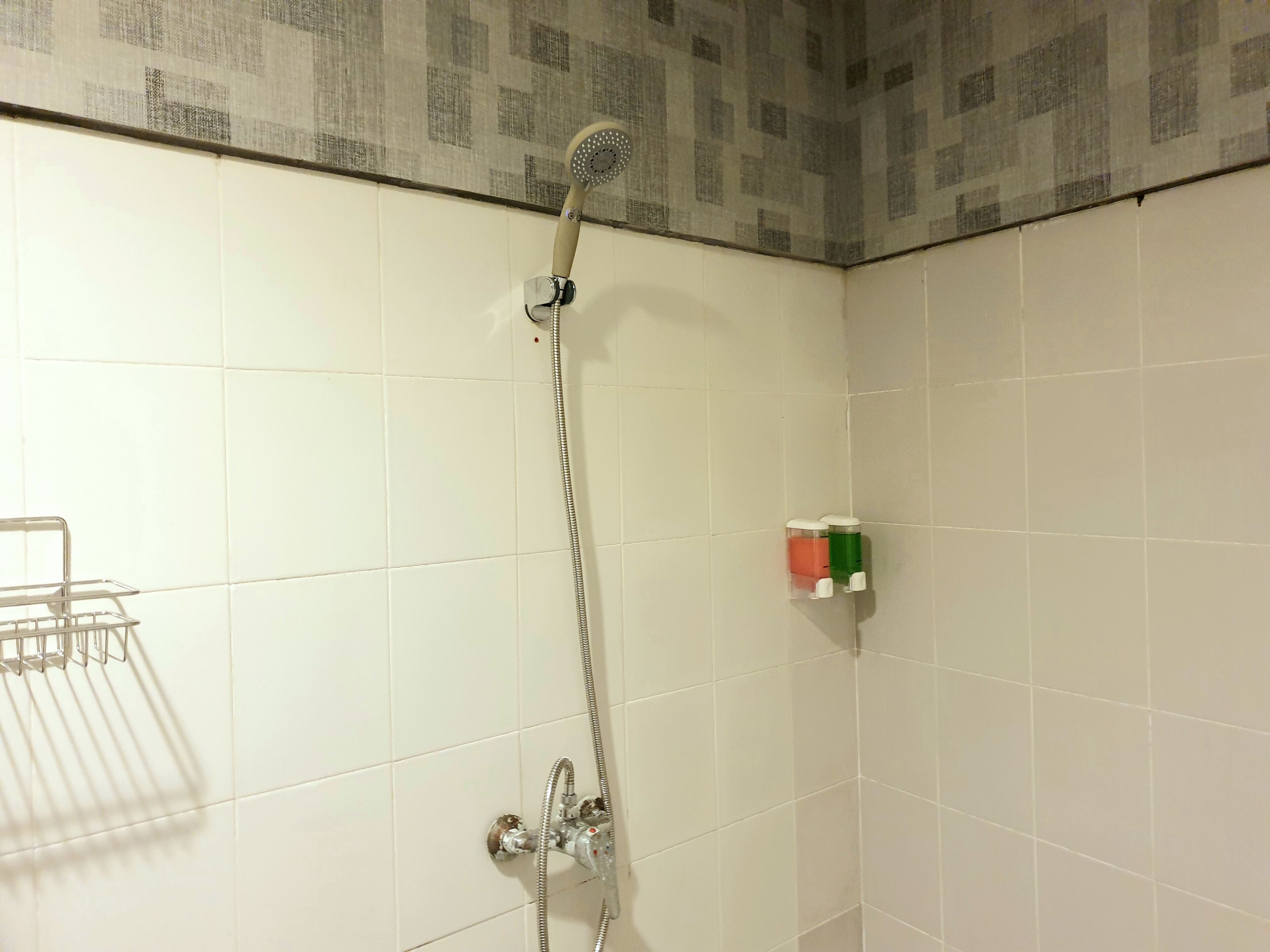 A bathroom with white tiled walls, a shower with a handheld showerhead, and a metal towel rack.