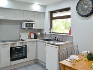 A compact kitchen with white cabinets, a microwave, a stove, and a sink. There is a window with a view of greenery outside.