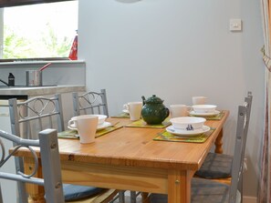 A dining table set with white cups, saucers, and a green teapot, surrounded by metal chairs.