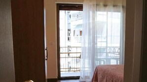 Habitación de hotel con suelo de madera, cama con edredón rosa y balcón con baranda de metal.