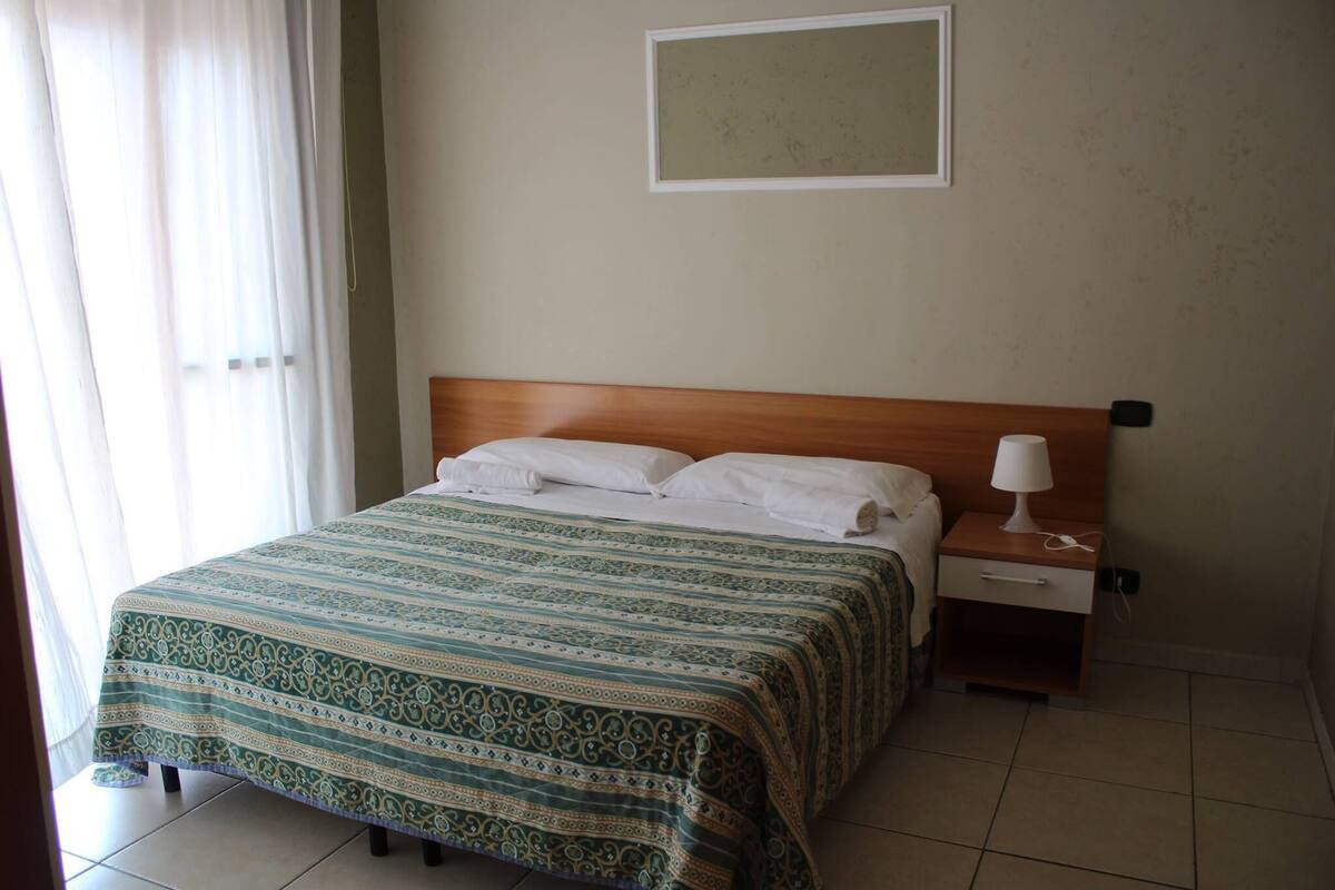 A neatly made bed with a patterned bedspread, a bedside table with a lamp, and a framed picture on the wall.
