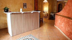 Un área de recepción con mostrador de madera, una planta en maceta, un letrero y piso de baldosas.