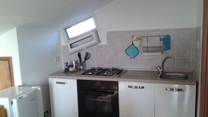 A compact kitchen with a gas stove, oven, and sink. There is a window above the stove and a small refrigerator to the left.