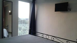 A hotel room with a bed, a TV mounted on the wall, and a balcony with a view.