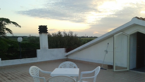 A rooftop patio with a table and chairs, a lamp post, and a view of the landscape.