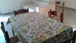 A dining area with a table covered by a fruit-patterned tablecloth, surrounded by wooden chairs.