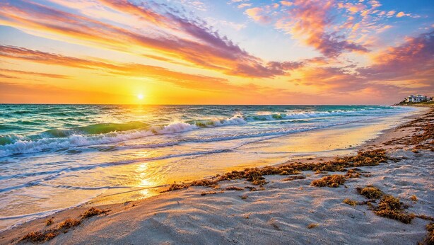 A beach with waves, a sunset, and a distant building.