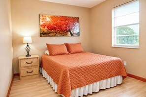 Une chambre à coucher avec un lit, une table de chevet, une lampe, un tableau et une fenêtre.